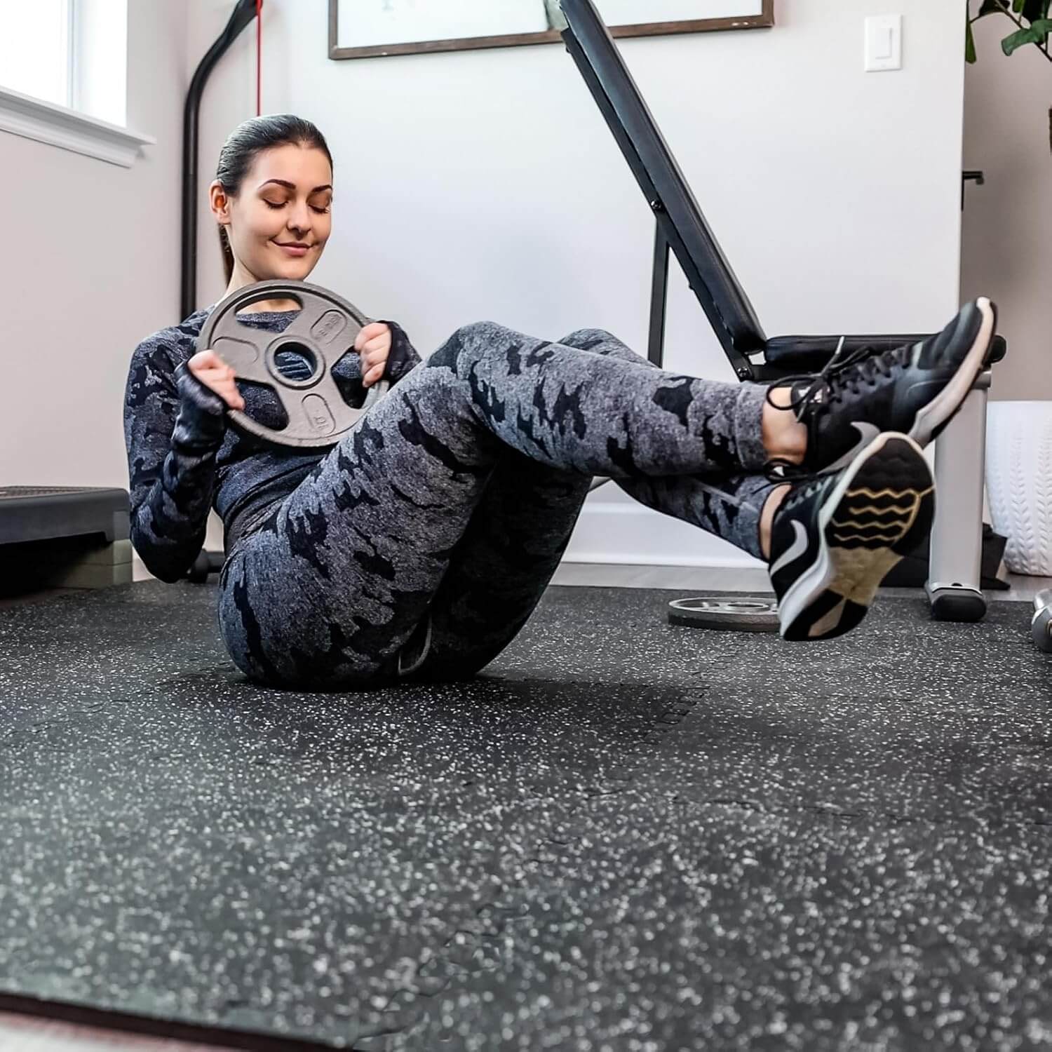 Woman doing exercises on Herbionyx FlexGuard Mats with a weight plate in a home gym setting.