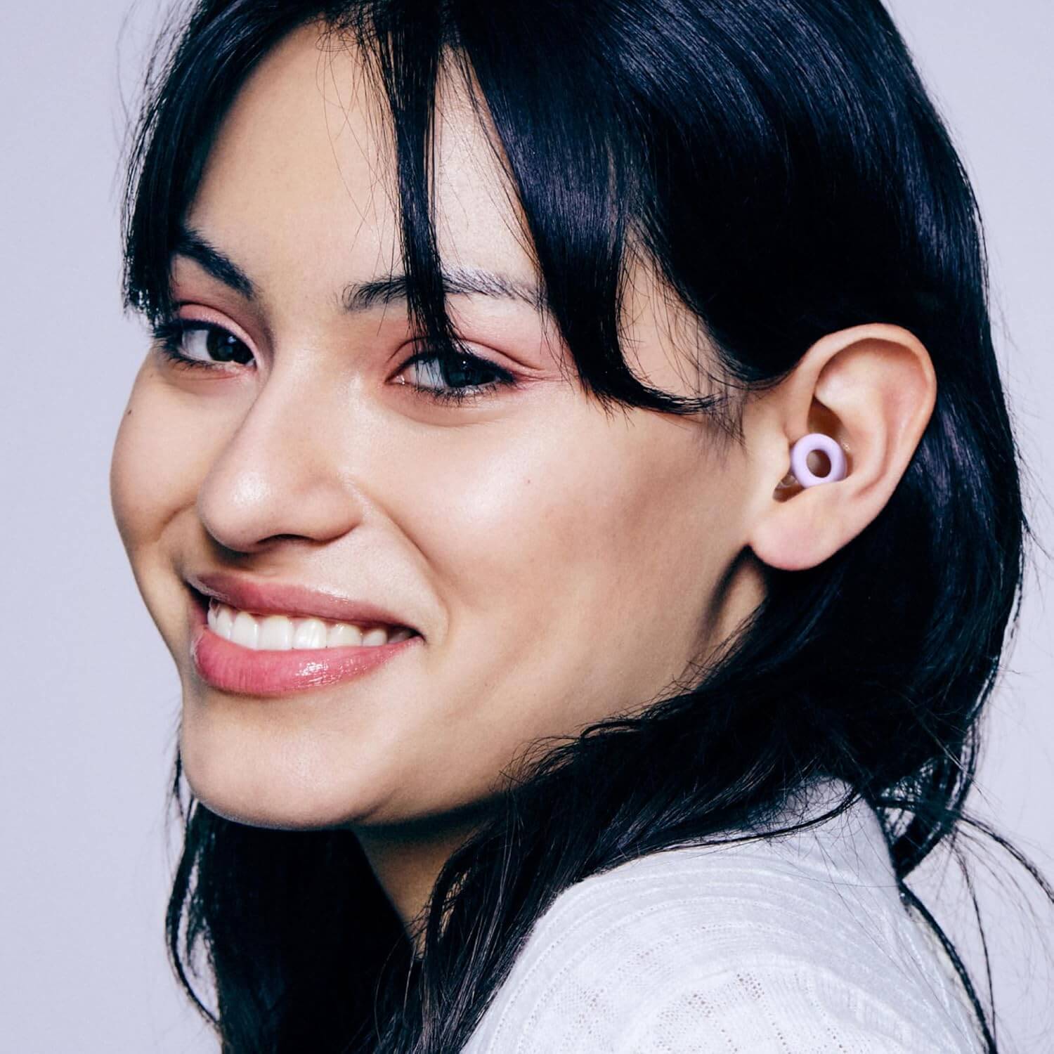Young woman wearing Herbionyx Quiet 2 earplugs, smiling with soft, flexible silicone ear tips for comfort.